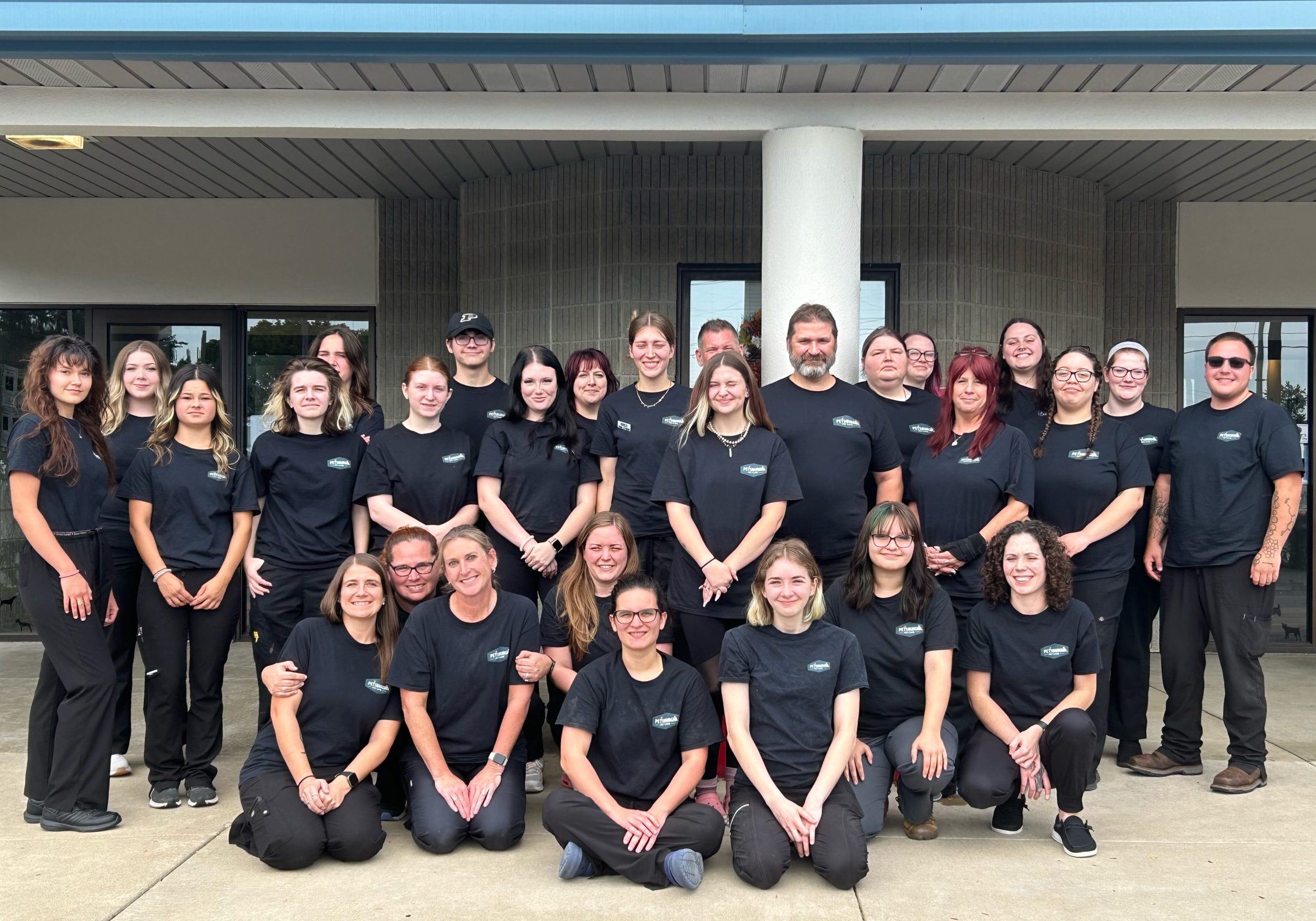 The entire vet team of Petsburgh Pet Care in Lafayette, IN standing in front of the building wearing black